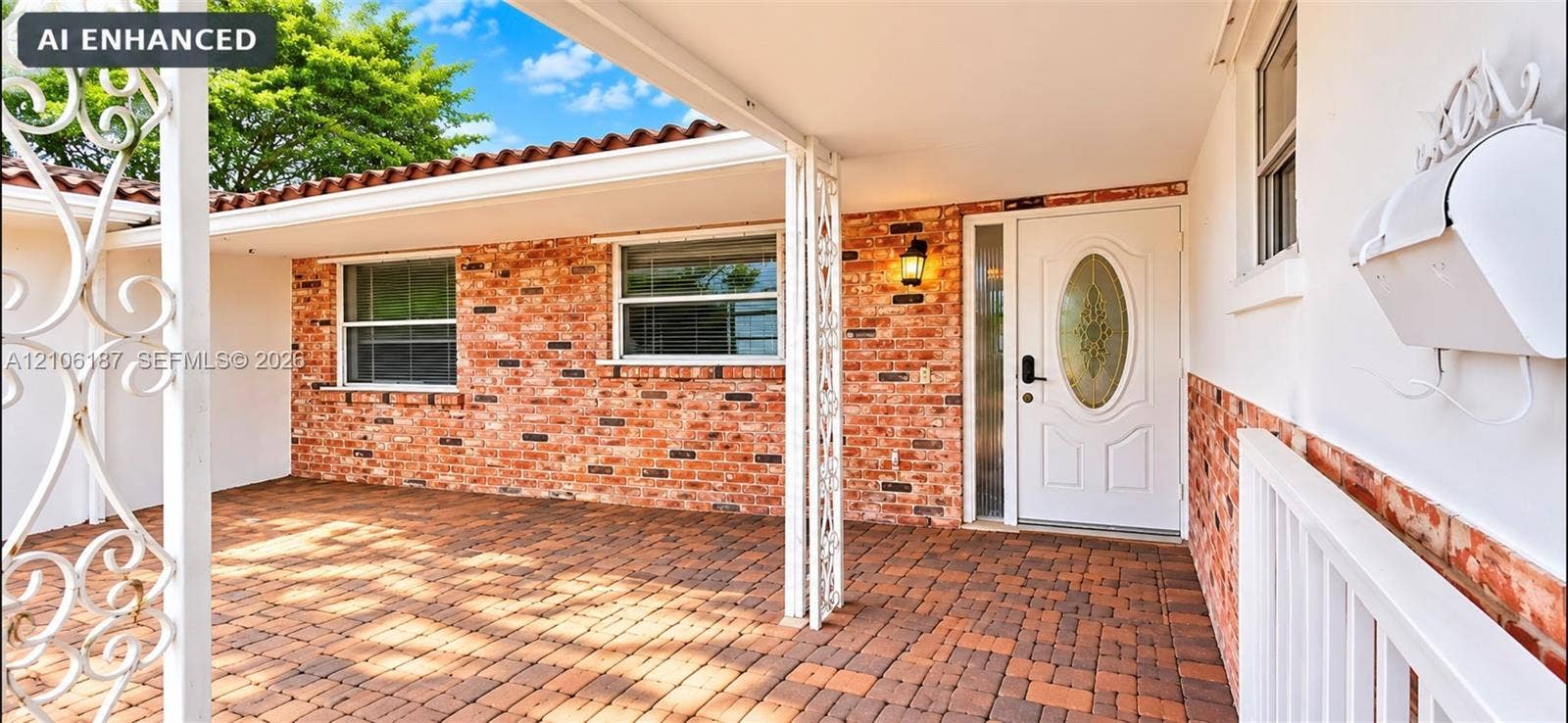 Covered front entry featuring red brick exterior siding, terracotta-style roof tiles, decorative metal porch supports, and a paved brick porch