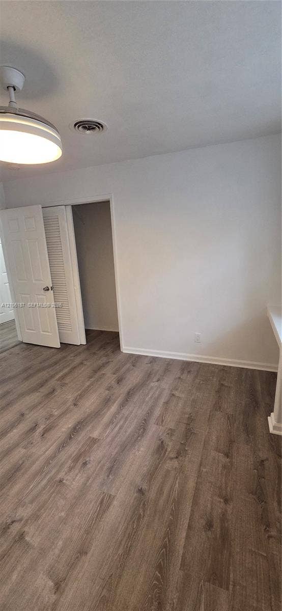 Interior space featuring wood-finish flooring, a neutral color palette, built-in closet with louvered doors, and a central ceiling-mounted light fixture