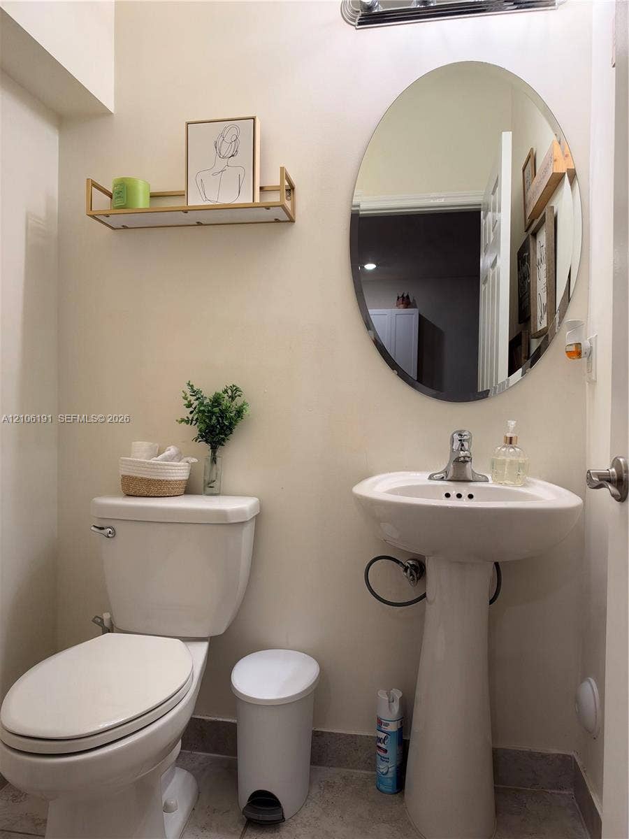 3402 W 105th Street, Hialeah, FL 33018 Pedestal sink with a single-handle faucet, oval wall-mounted mirror, and wall-mounted metal shelf