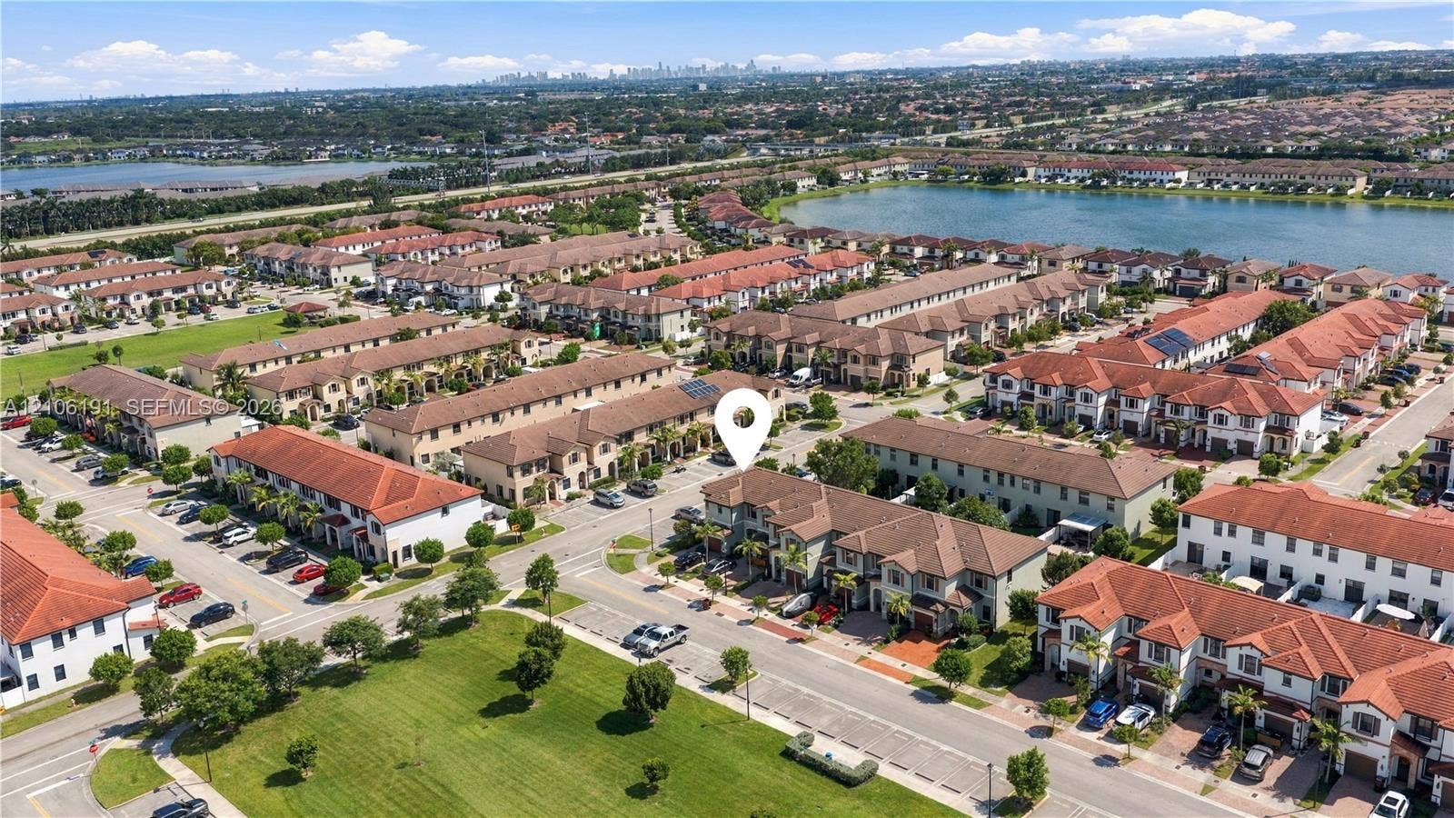 3402 W 105th Street, Hialeah, FL 33018 Aerial perspective of a multi-story residence featuring a terracotta-tiled roof and stucco exterior, situated within a community highlighted by expansive water frontage and manicured green spaces