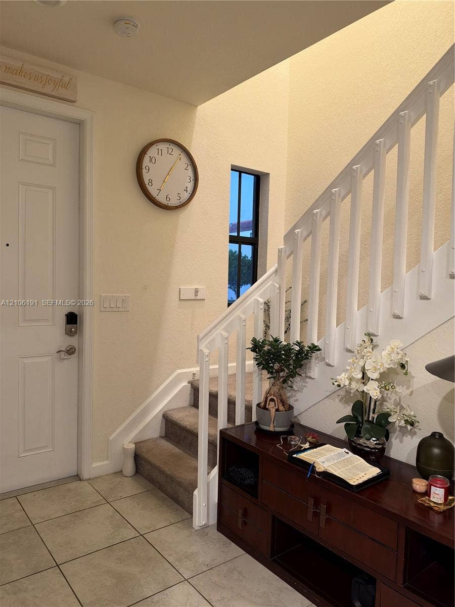 3402 W 105th Street, Hialeah, FL 33018 Entryway featuring ceramic tile flooring, a painted white staircase with a vertical balustrade, carpeted stair treads, and a multi-pane window