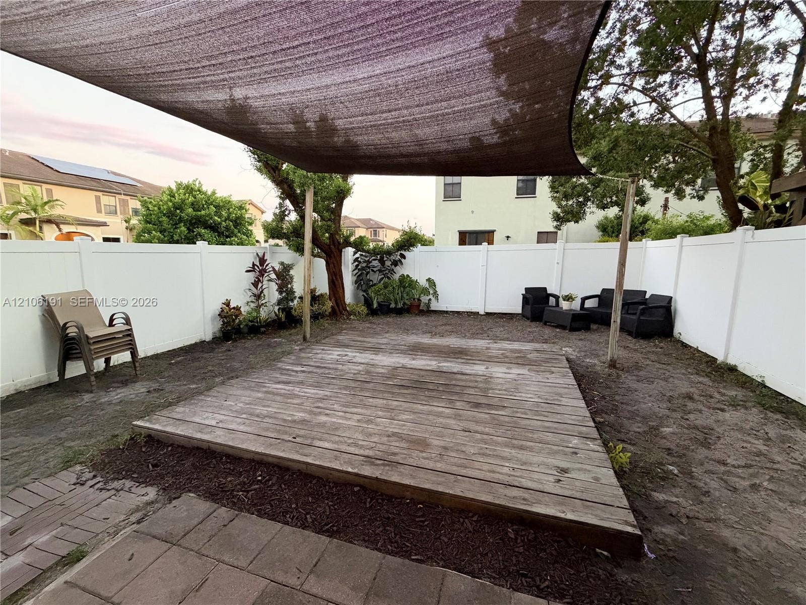 3402 W 105th Street, Hialeah, FL 33018 Backyard featuring a wood deck, a tensioned shade canopy, a white vinyl privacy fence, and brick paver accents