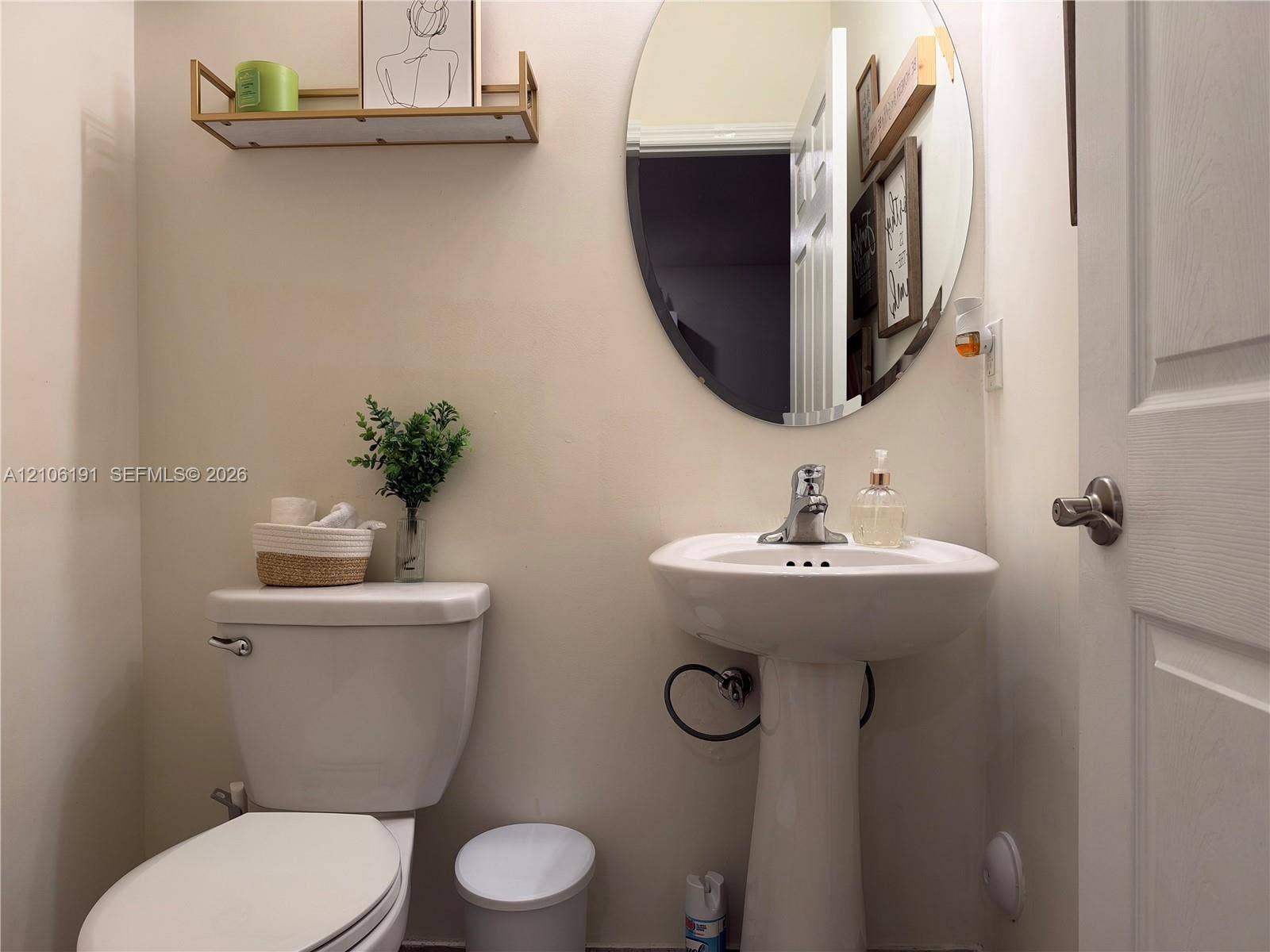 3402 W 105th Street, Hialeah, FL 33018 Oval wall-mounted mirror, white pedestal sink with chrome faucet, and fixed wall-mounted shelving