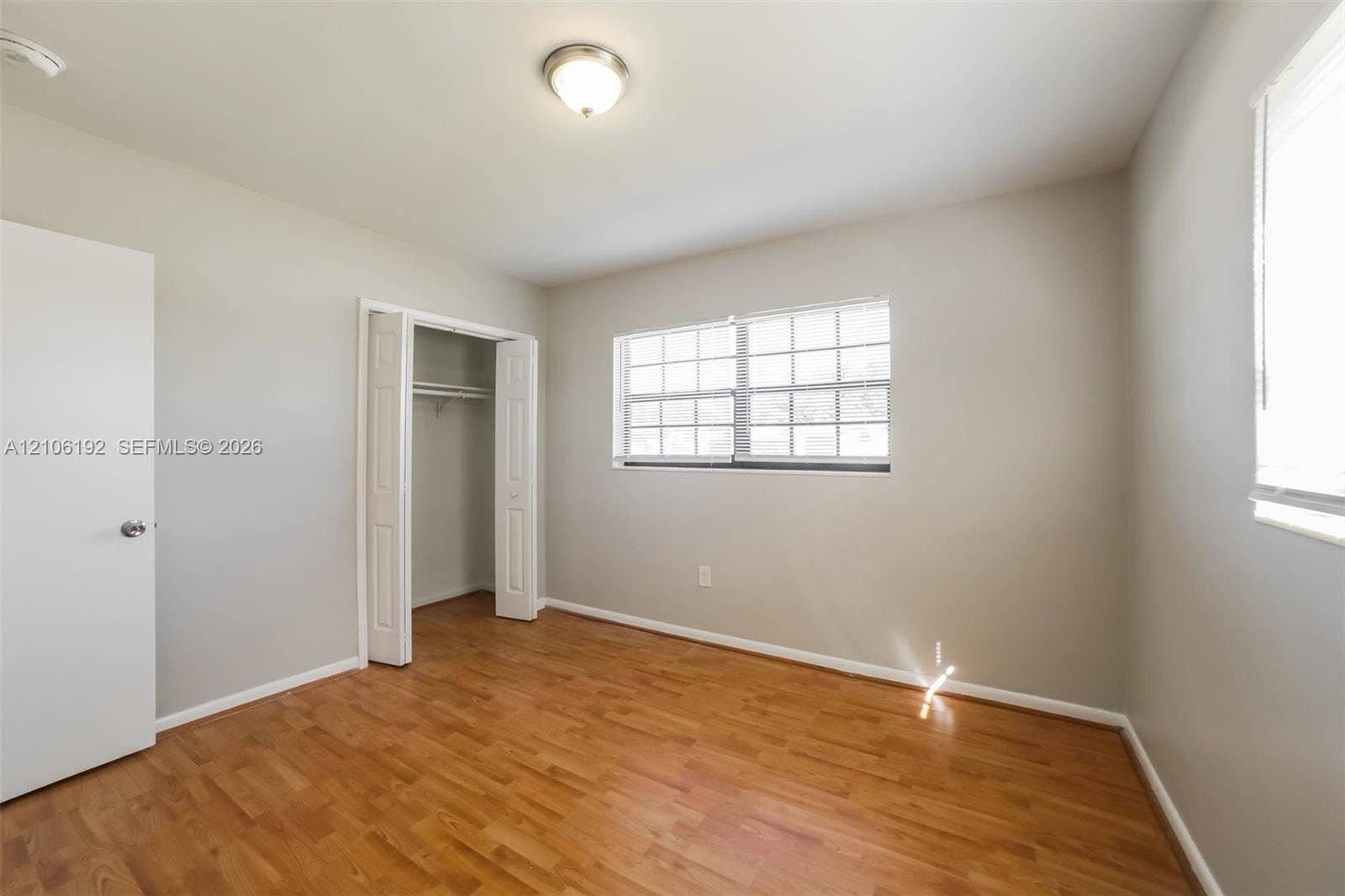 19100 NW 12th Avenue, Miami Gardens, Miami Gardens, FL 33169 Room featuring wood-finish flooring, neutral wall paint, a multi-pane window with white trim, and a closet with bifold doors