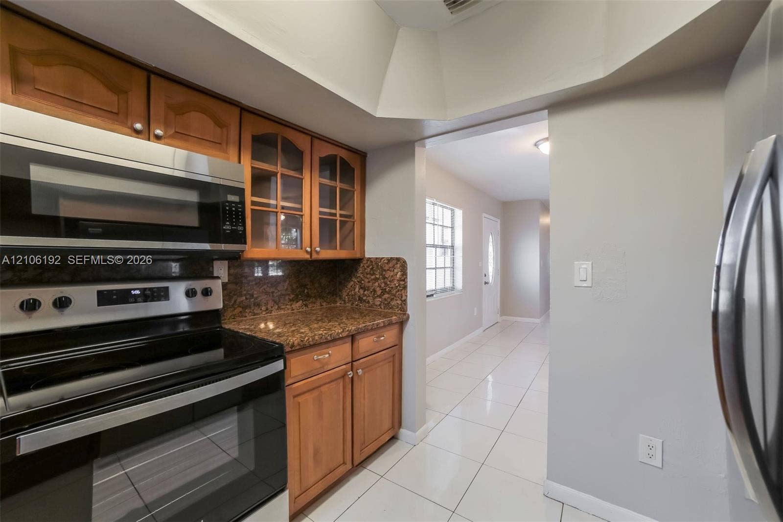 19100 NW 12th Avenue, Miami Gardens, Miami Gardens, FL 33169 Kitchen featuring natural-finish wood cabinetry with glass-front display panels, speckled stone-finish countertops, stainless steel appliances, and a vaulted ceiling