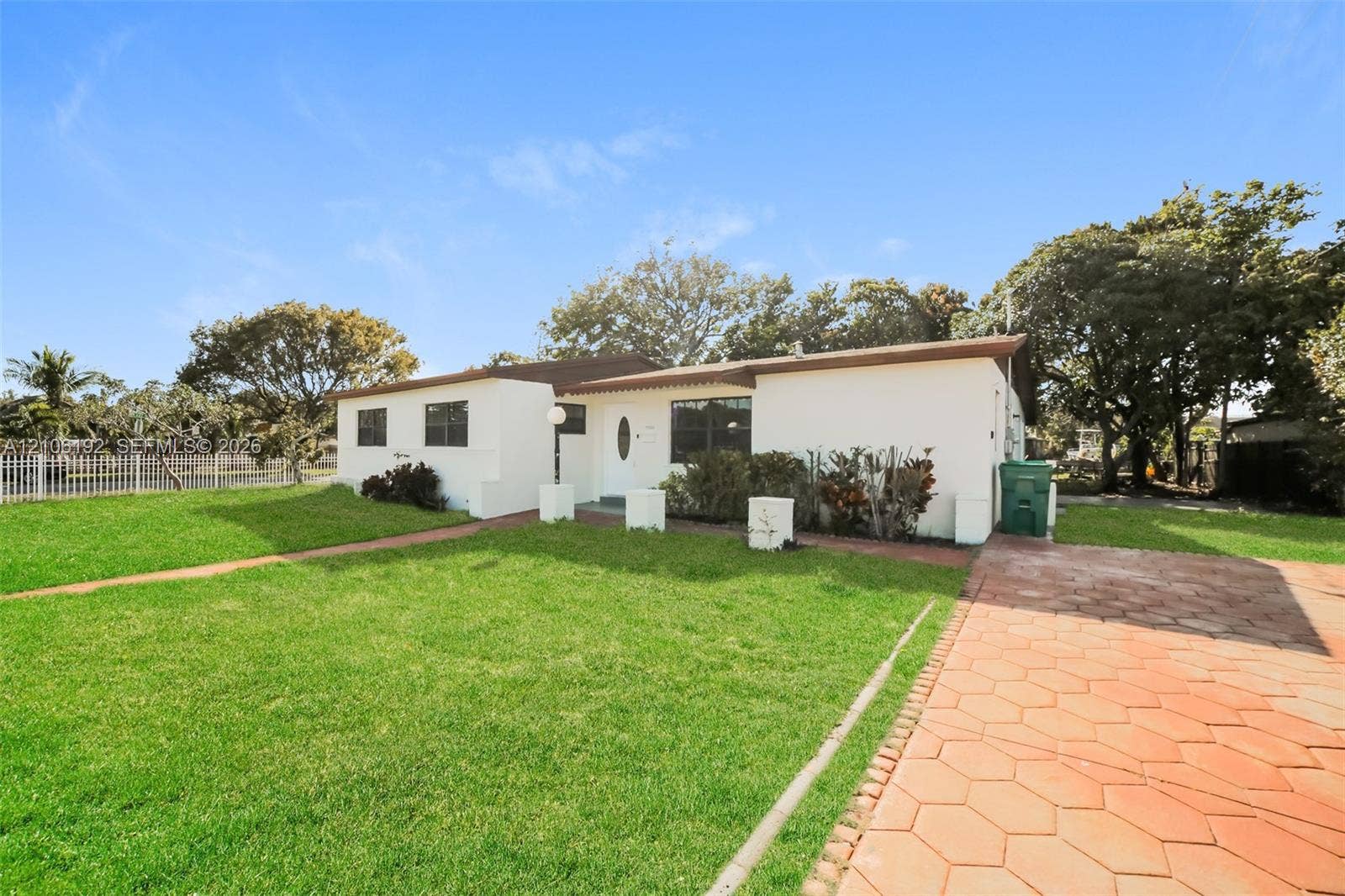 19100 NW 12th Avenue, Miami Gardens, Miami Gardens, FL 33169 Single-story residence featuring a smooth stucco exterior, low-pitch roofline, expansive manicured lawn, and a hexagonal paver driveway
