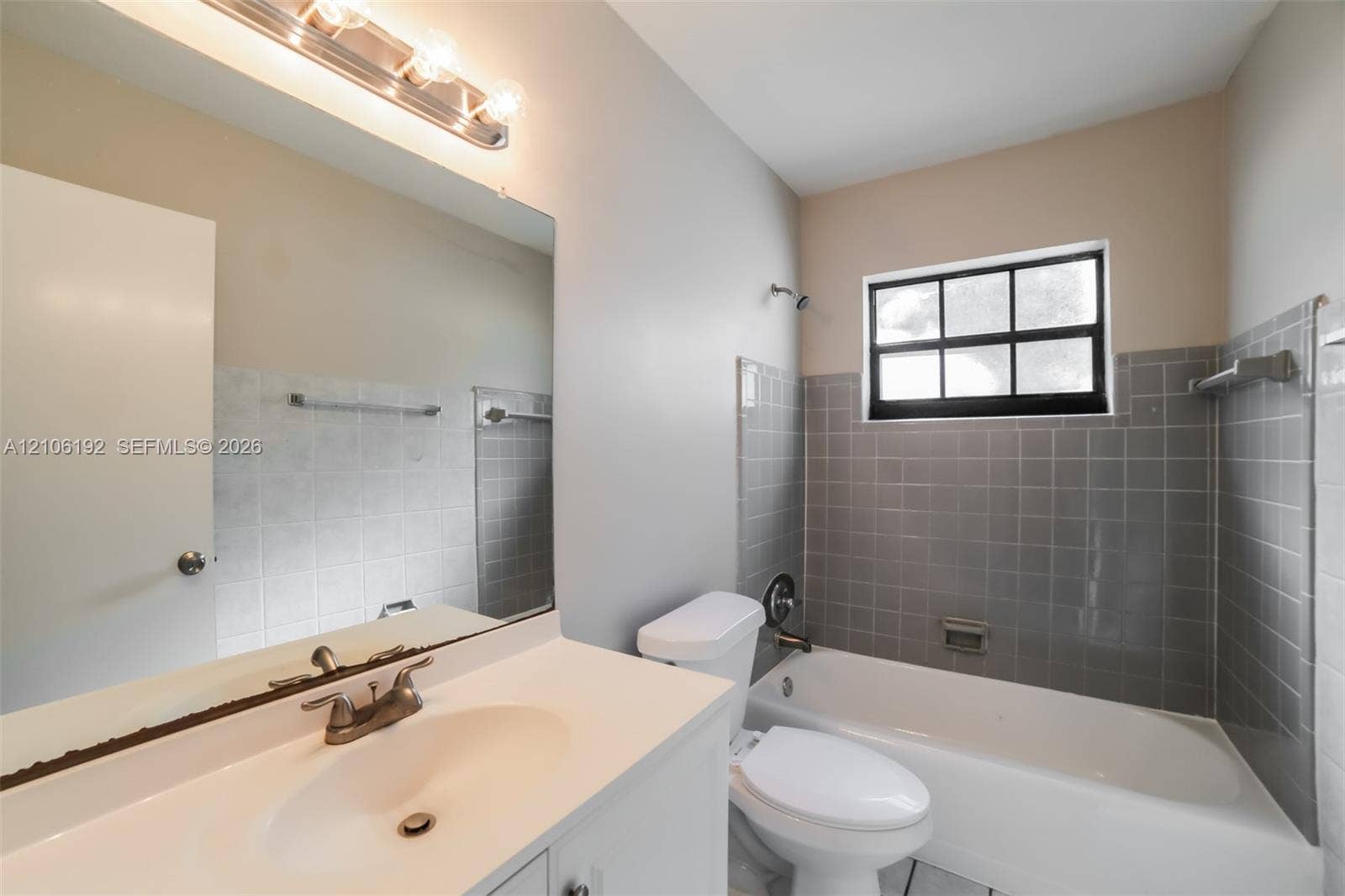 19100 NW 12th Avenue, Miami Gardens, Miami Gardens, FL 33169 Bathroom featuring a vanity with integrated sink, expansive wall-mounted mirror, multi-bulb light fixture, and a tub-shower combination with gray tile surround and window
