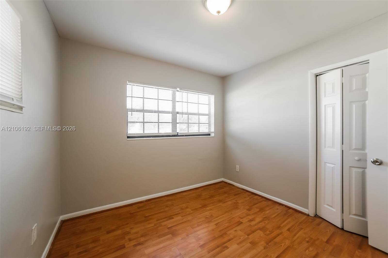 19100 NW 12th Avenue, Miami Gardens, Miami Gardens, FL 33169 Room featuring wood-finish flooring, neutral wall paint, a multi-pane window, and a closet with paneled bifold doors