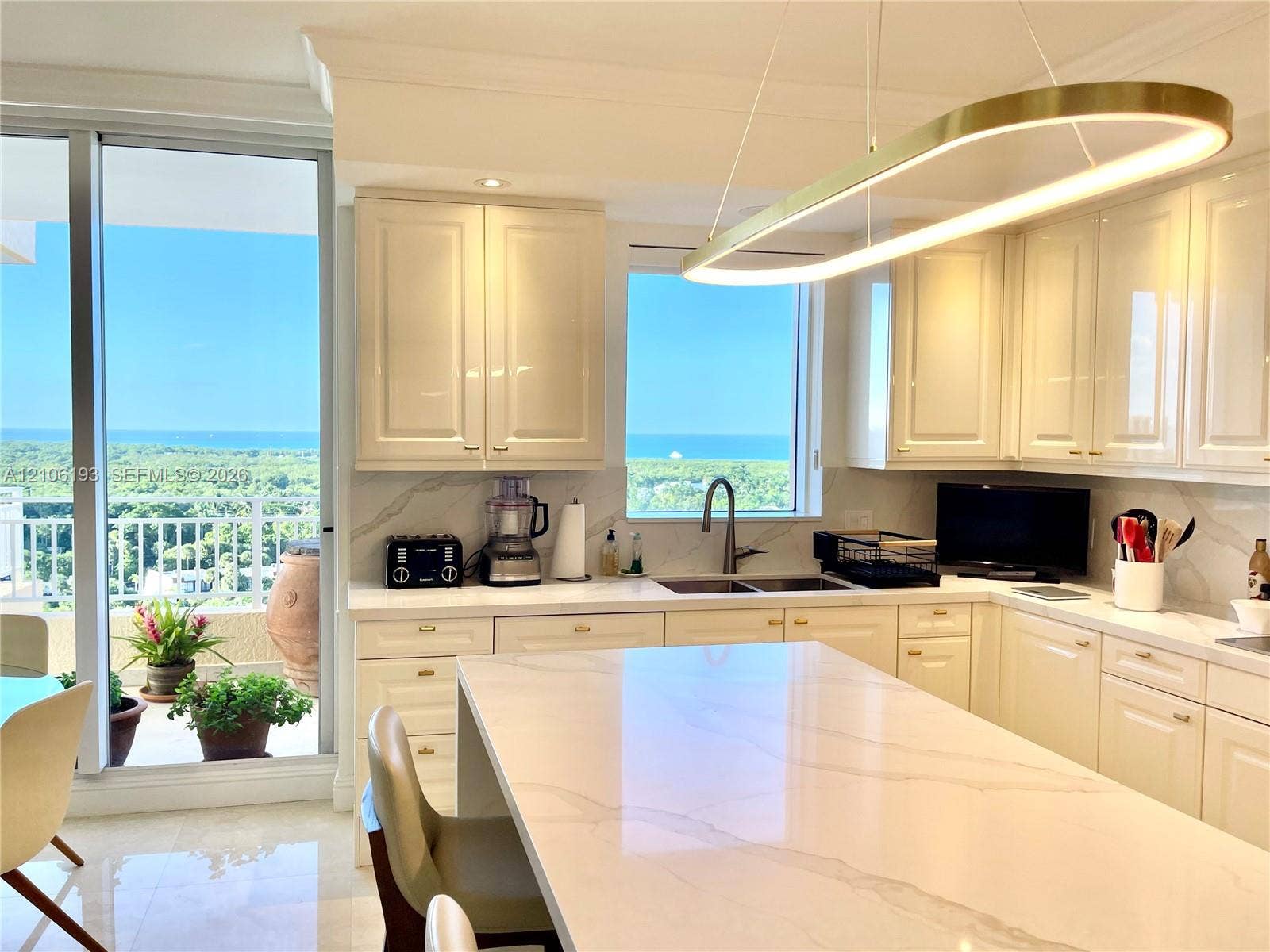 799 Crandon Boulevard, #1203, Key Biscayne, Key Biscayne, FL 33149 Kitchen featuring glossy cream cabinetry, a central island with a stone countertop, an integrated stainless steel dual-basin sink, and a circular LED pendant light fixture