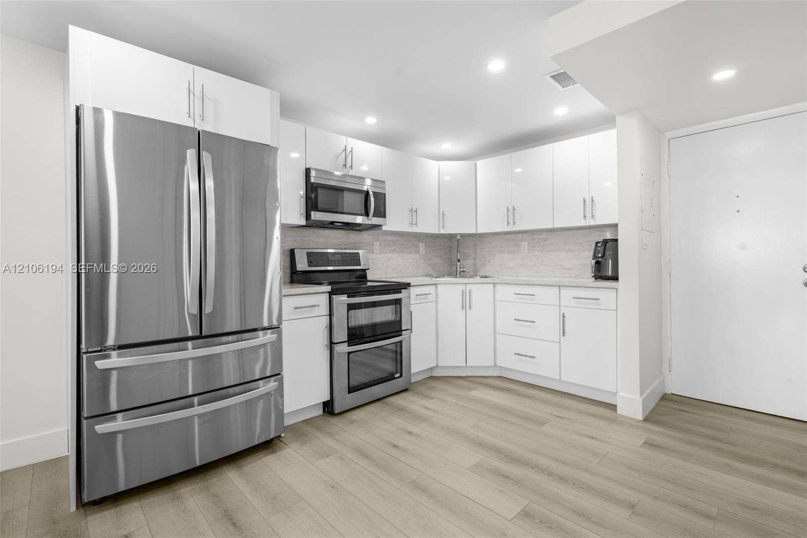 777 SW 9th Avenue, #408, Miami, FL 33130 Kitchen featuring white cabinetry, stainless steel appliances, wood-finish flooring, recessed lighting, and a light-toned backsplash