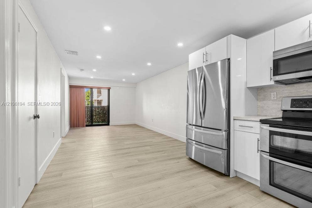777 SW 9th Avenue, #408, Miami, FL 33130 Modern kitchen featuring white flat-panel cabinetry, stainless steel appliances, wood-finish flooring, and recessed ceiling lighting