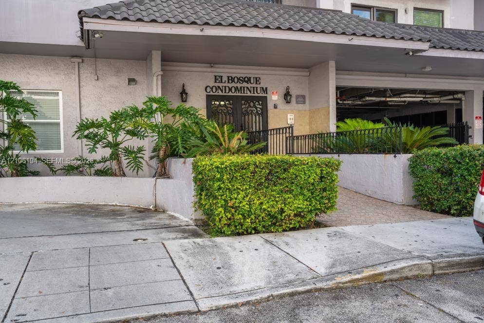 777 SW 9th Avenue, #408, Miami, FL 33130 Exterior facade featuring a covered entryway with decorative metal double doors, tile roofing, integrated wall-mounted lighting, and curated shrubbery