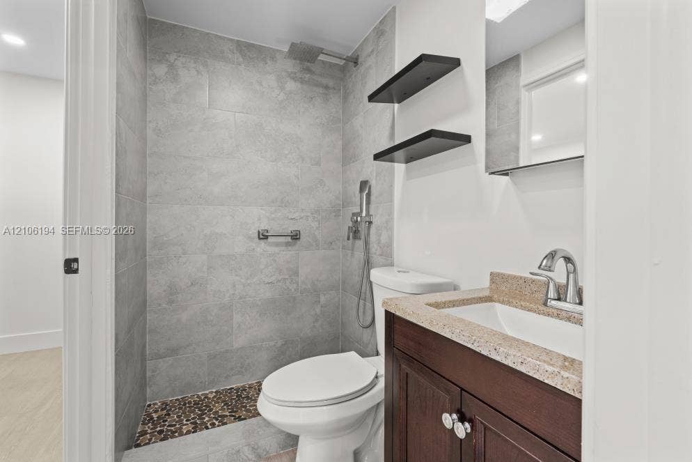 777 SW 9th Avenue, #408, Miami, FL 33130 Walk-in shower featuring gray stone-finish tile surround, integrated pebble tile floor, and rainfall showerhead, complemented by a dark wood-finish vanity with a stone-finish countertop, dual-handle faucet, and built-in wall shelving