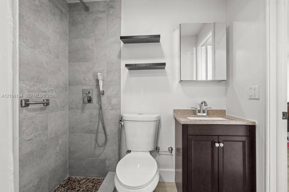 777 SW 9th Avenue, #408, Miami, FL 33130 Bathroom featuring a walk-in shower with stone-style tile surround and pebble tile flooring, dark-finish cabinetry with a speckled countertop, wall-mounted medicine cabinet, and built-in wall shelving