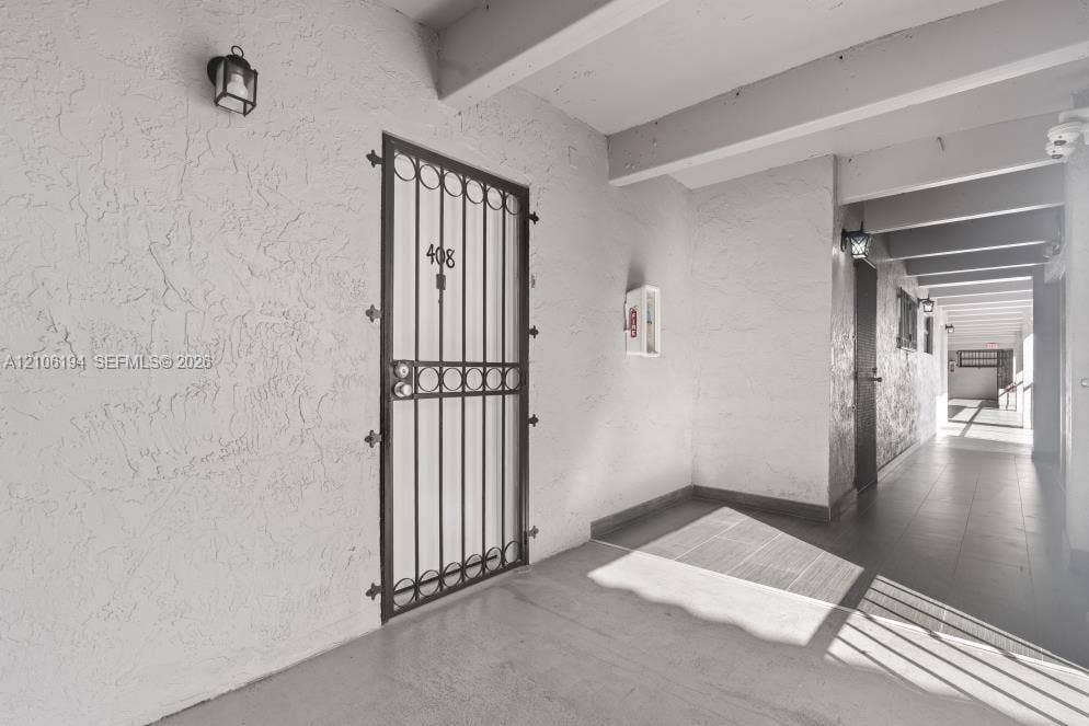 777 SW 9th Avenue, #408, Miami, FL 33130 Covered exterior walkway featuring textured stucco walls, concrete flooring, decorative metal security door, and wall-mounted exterior lanterns