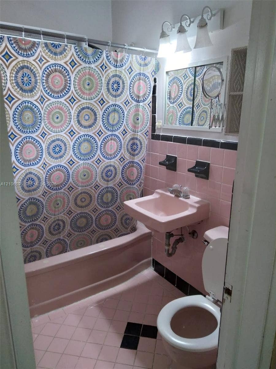 8132 Harding Avenue, #11, Miami Beach, Miami Beach, FL 33141 Bathroom featuring pink wall tiling with black accent trim, wall-mounted sink, built-in shelving, and a three-light vanity fixture