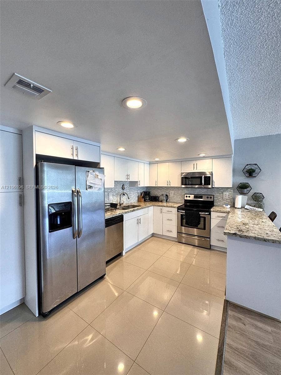 Kitchen featuring white cabinetry, stone-surface countertops, recessed lighting, stainless steel appliances, and large-format tile flooring
