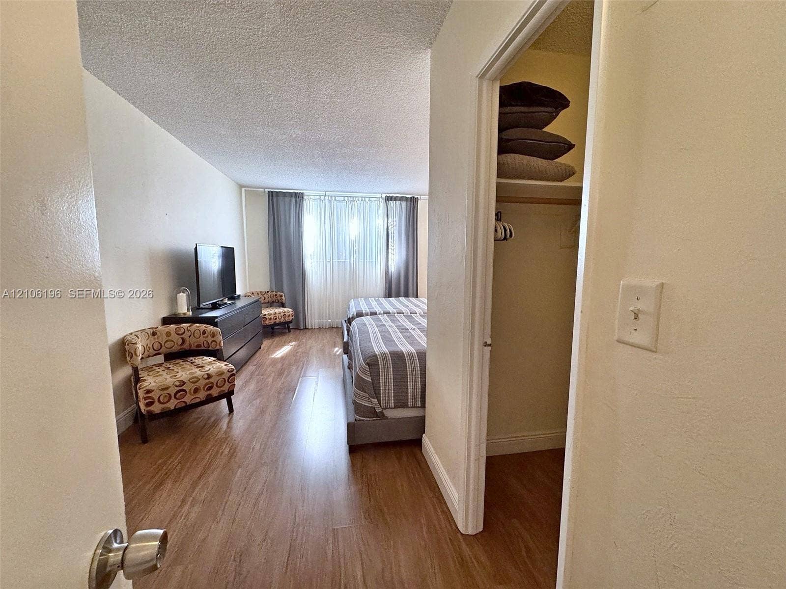 Wood-finish flooring throughout, walk-in closet with built-in shelving, and large windows with integrated track curtains