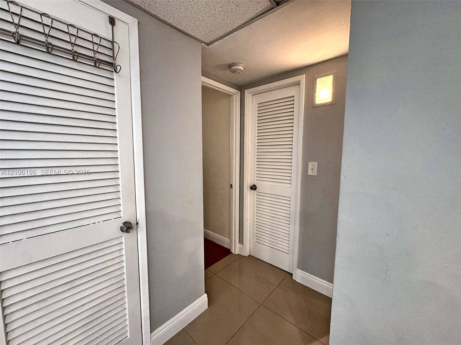 Neutral-toned interior featuring large-format tile flooring, white louvered closet doors, and a wall-mounted sconce