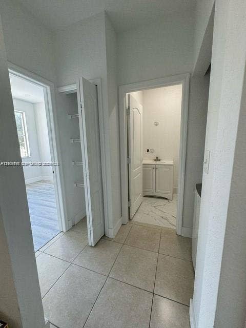 17660 NW 73rd Avenue, #202-3, Hialeah, Hialeah, FL 33015 Hallway featuring large-format tile flooring, a dedicated storage closet with built-in shelving, and entry to a bathroom finished with light stone-patterned flooring and a vanity cabinet
