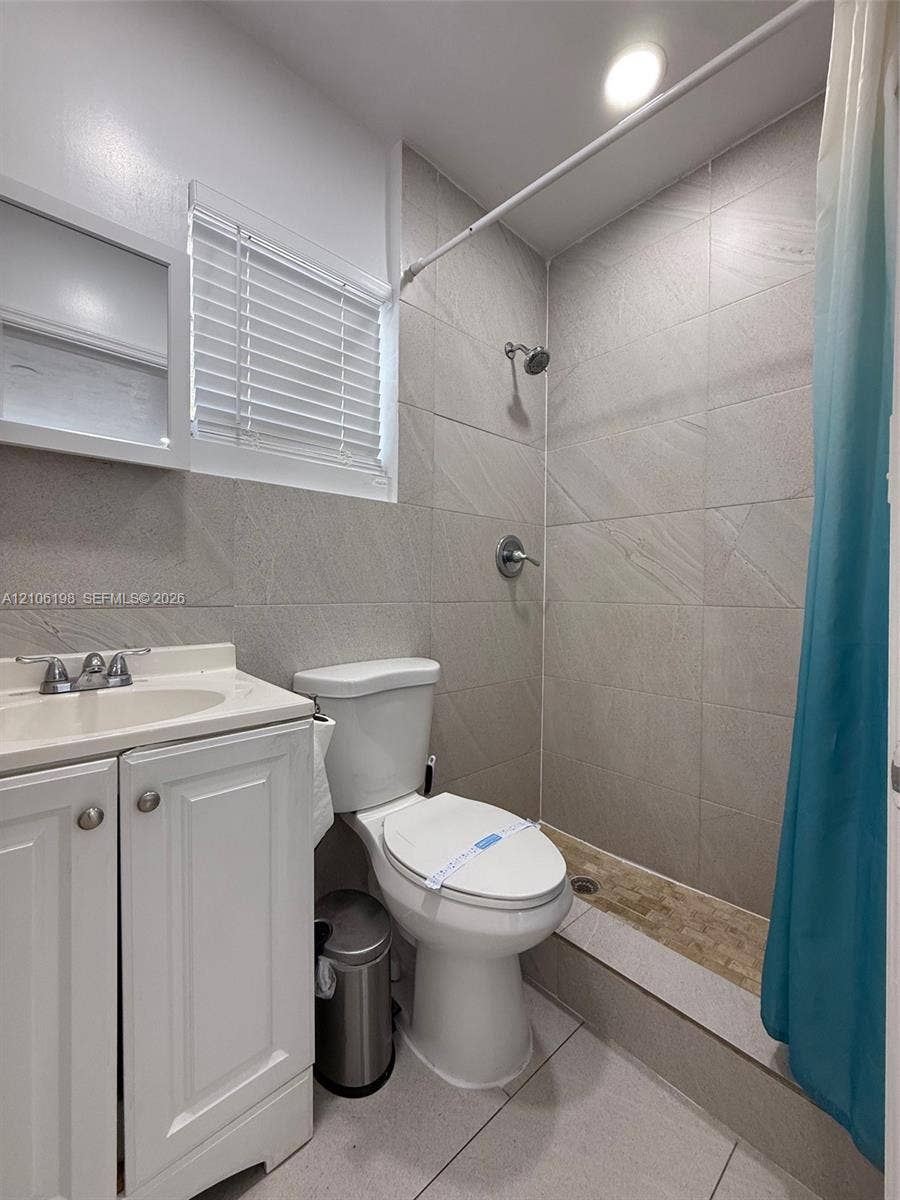 600 NW 116th Terrace, Miami, FL 33168 Bathroom featuring white cabinetry, large-format tile wall surround, recessed shower area with stone-finish flooring, and integrated medicine cabinet