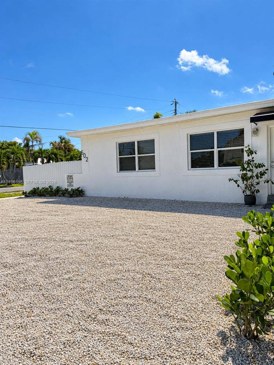 600 NW 116th Terrace, Miami, FL 33168 Exterior featuring a white stucco facade, gravel driveway, and white vinyl privacy fencing