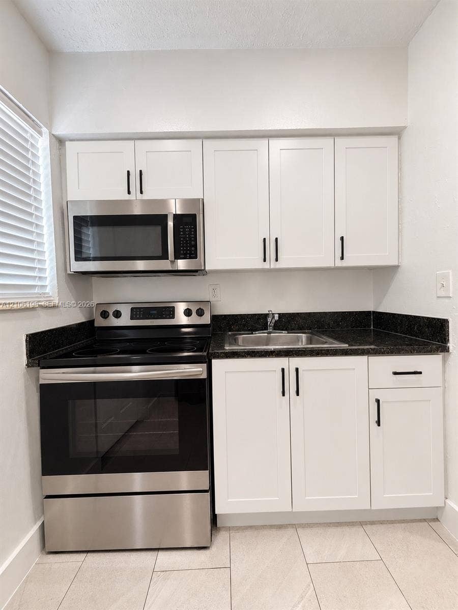 600 NW 116th Terrace, Miami, FL 33168 Kitchen area featuring white shaker-style cabinetry, dark stone-finish countertops, stainless steel appliances, and large-format neutral floor tile
