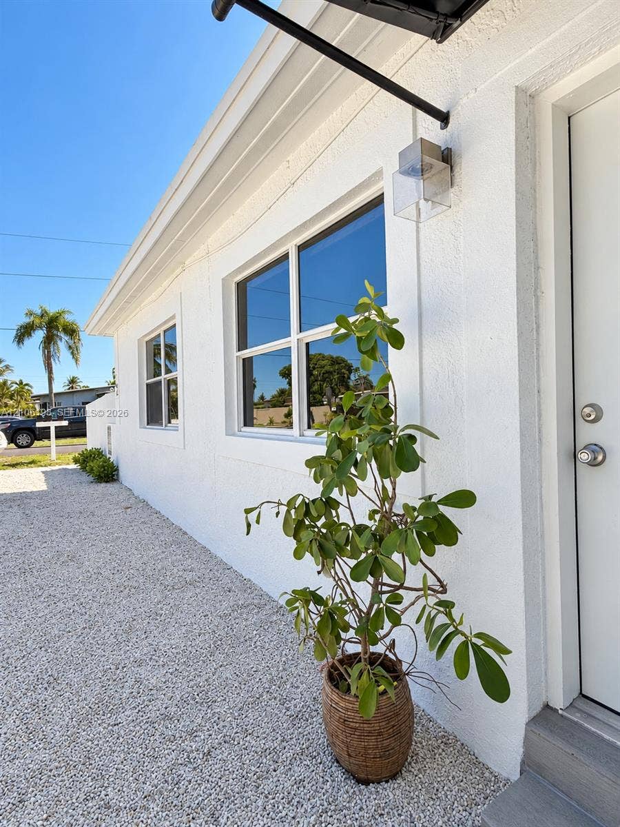 600 NW 116th Terrace, Miami, FL 33168 Stucco exterior featuring dual-pane windows, a metal door with brushed nickel hardware, and a minimalist wall-mounted outdoor light fixture