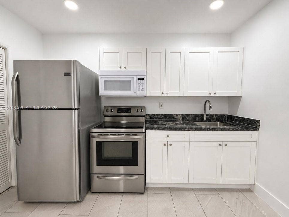 600 NW 116th Terrace, Miami, FL 33168 Kitchen featuring white shaker-style cabinetry, dark stone-finish countertops, stainless steel appliances, a mounted microwave, and ceramic tile flooring