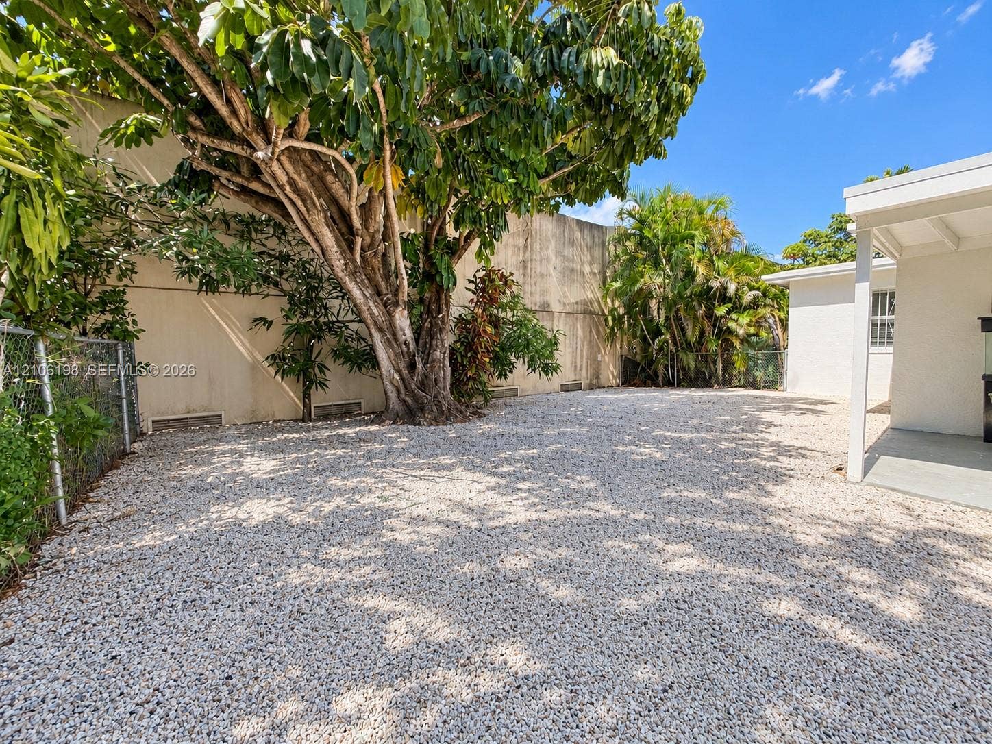 600 NW 116th Terrace, Miami, FL 33168 Low-maintenance gravel yard featuring a concrete patio, mature shade tree, and perimeter fencing
