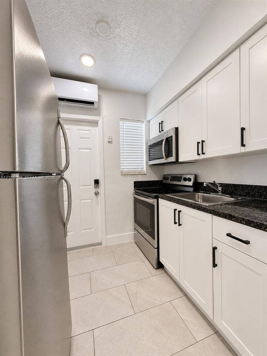 600 NW 116th Terrace, Miami, FL 33168 Kitchen featuring white shaker-style cabinetry, stainless steel appliances, dark countertops, tile flooring, and a wall-mounted ductless climate control unit