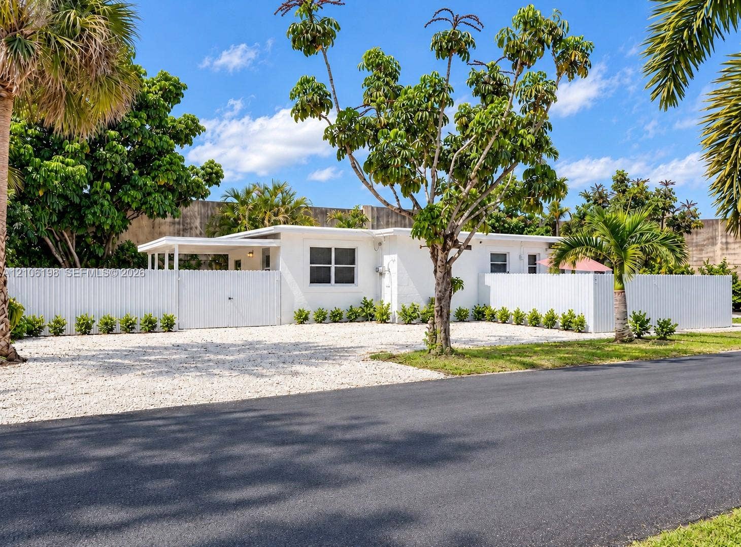 600 NW 116th Terrace, Miami, FL 33168 Single-story residence featuring white exterior cladding, a covered entryway, an expansive gravel front area, and a privacy fence