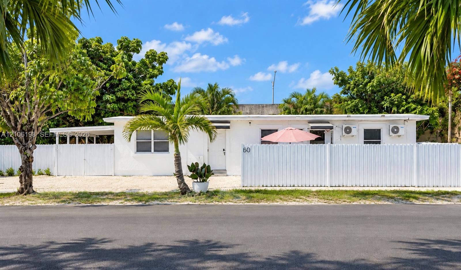 600 NW 116th Terrace, Miami, FL 33168 Single-story exterior featuring white stucco siding, a gravel driveway, an attached carport, and full-perimeter privacy fencing