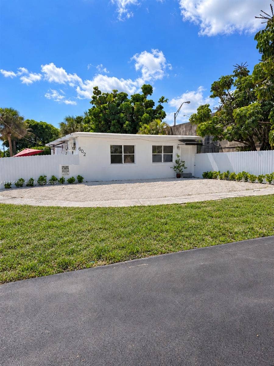 600 NW 116th Terrace, Miami, FL 33168 Single-story residence featuring a crisp white exterior, gravel front courtyard, horizontal slat privacy fencing, and manicured lawn
