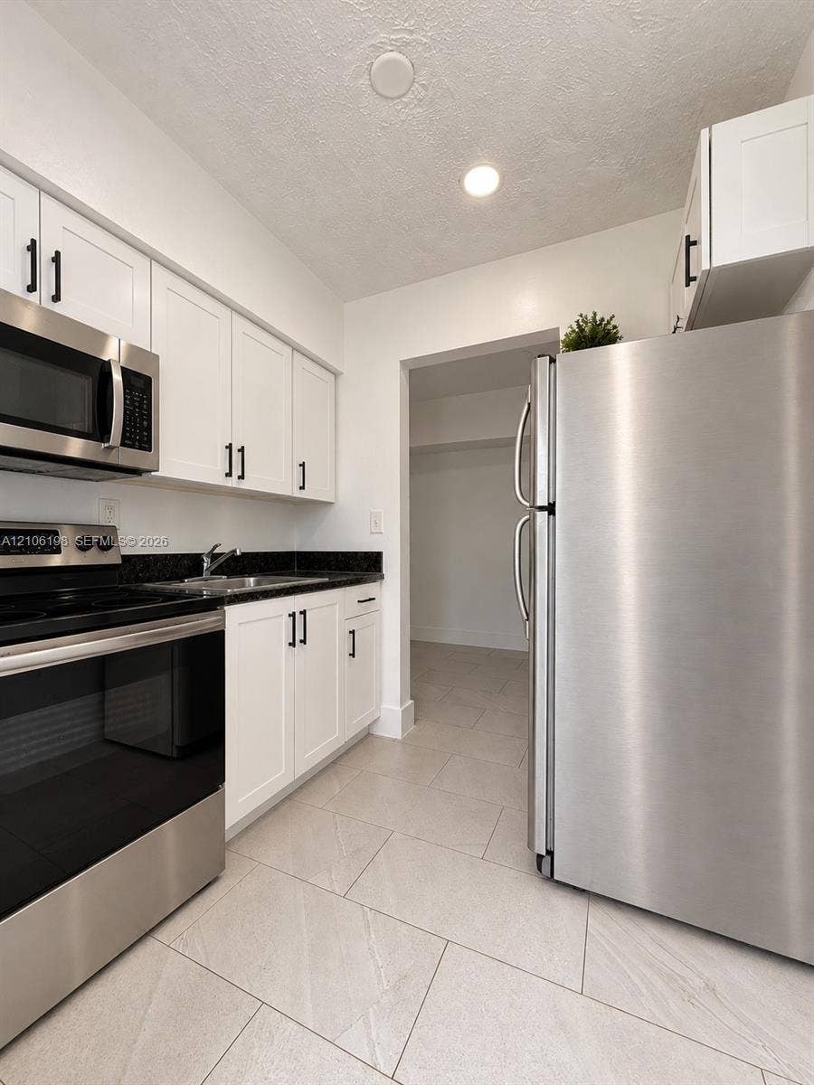 600 NW 116th Terrace, Miami, FL 33168 Kitchen featuring white cabinetry with matte black hardware, dark stone-finish countertops, stainless steel appliances, and large-format tile flooring