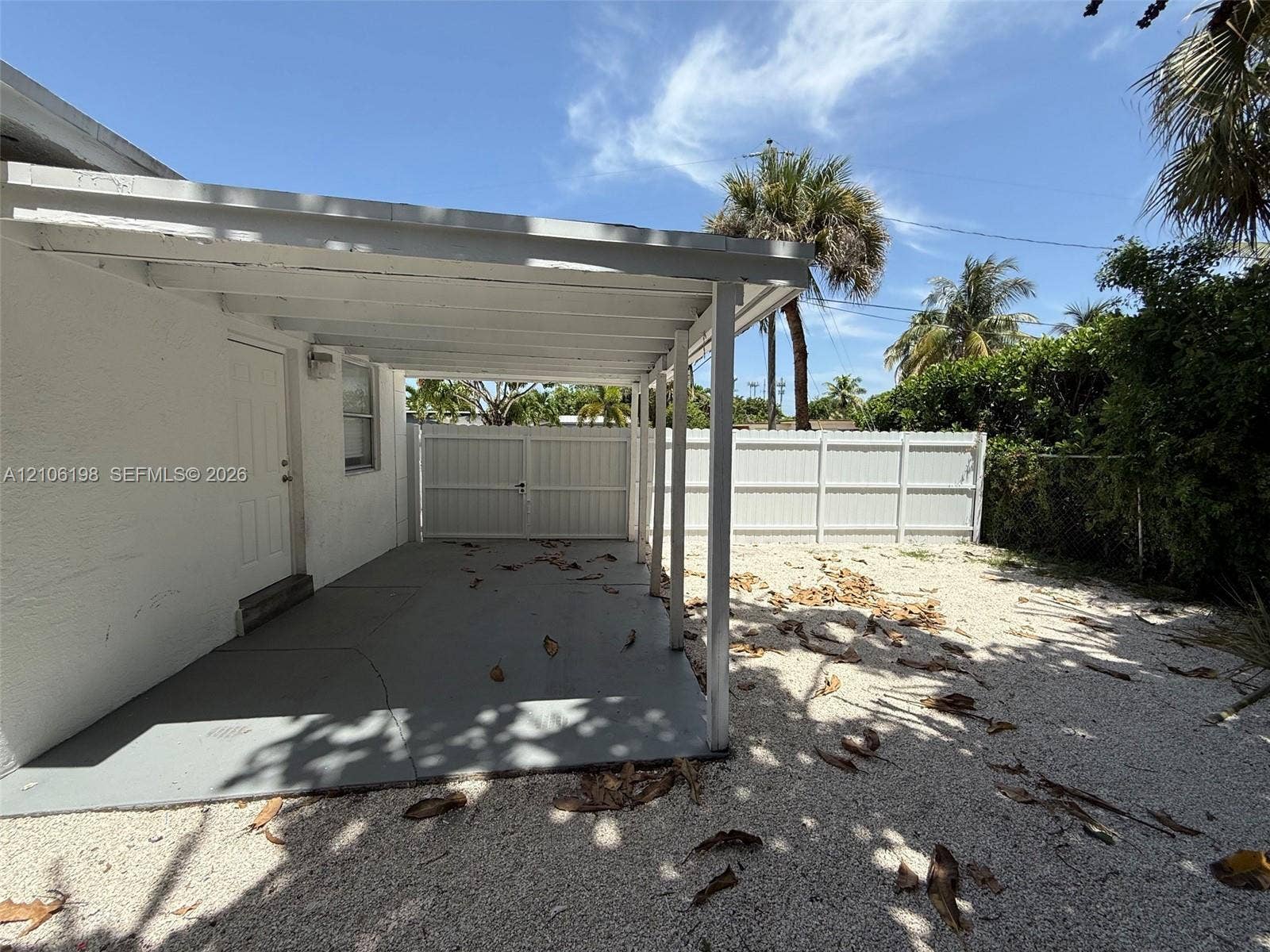 600 NW 116th Terrace, Miami, FL 33168 Covered concrete patio with white support beams, exterior entry door, and white privacy fencing enclosing a stone-ground yard
