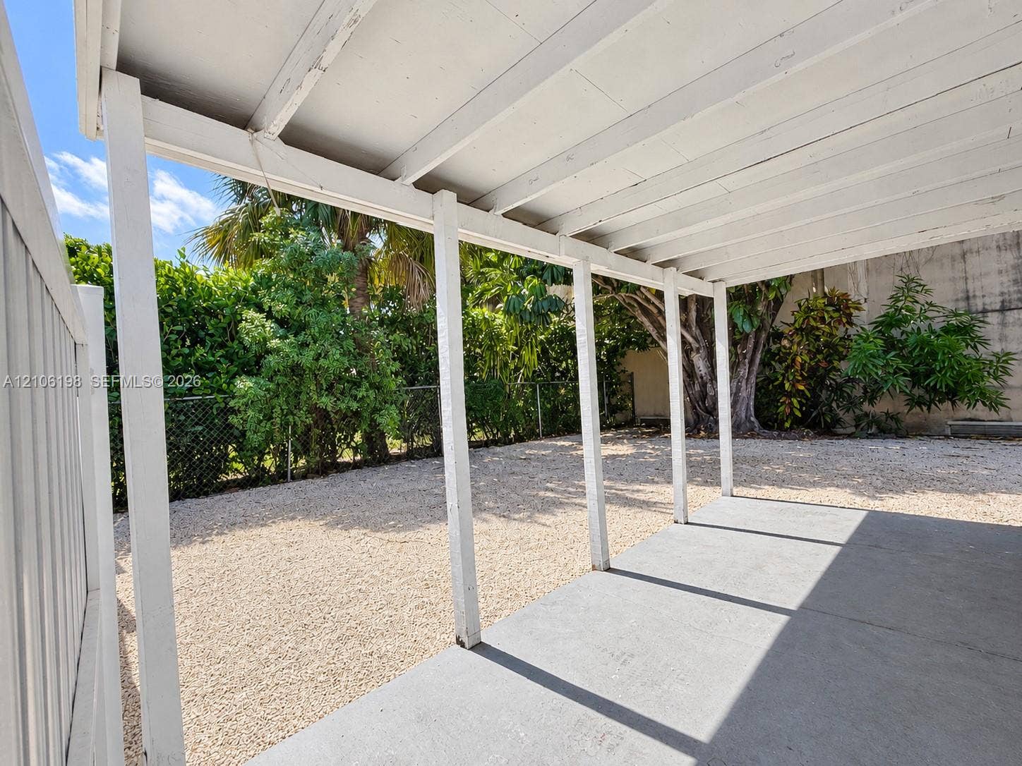 600 NW 116th Terrace, Miami, FL 33168 Covered concrete patio featuring a white support structure, gravel yard, and perimeter chain-link fencing