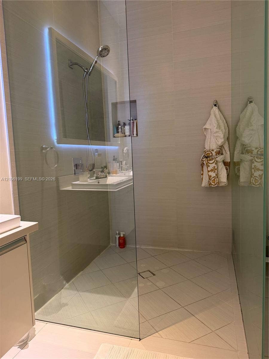 Walk-in shower featuring a frameless glass enclosure, neutral tile surround, built-in wall niche, overhead shower head, and tiled flooring