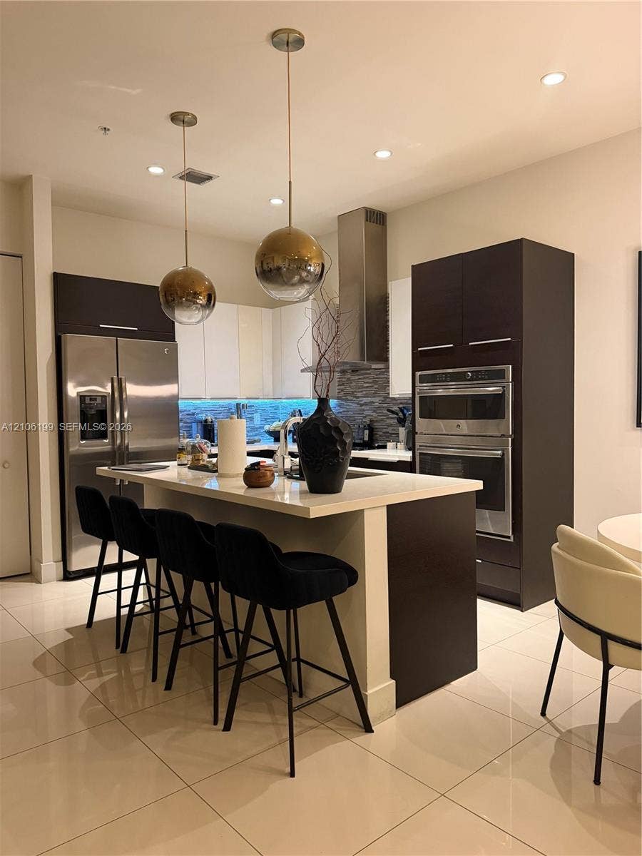 Kitchen featuring custom flat-panel cabinetry, a central island with stone-finish countertops, stainless steel built-in double wall ovens, recessed lighting, and spherical pendant fixtures