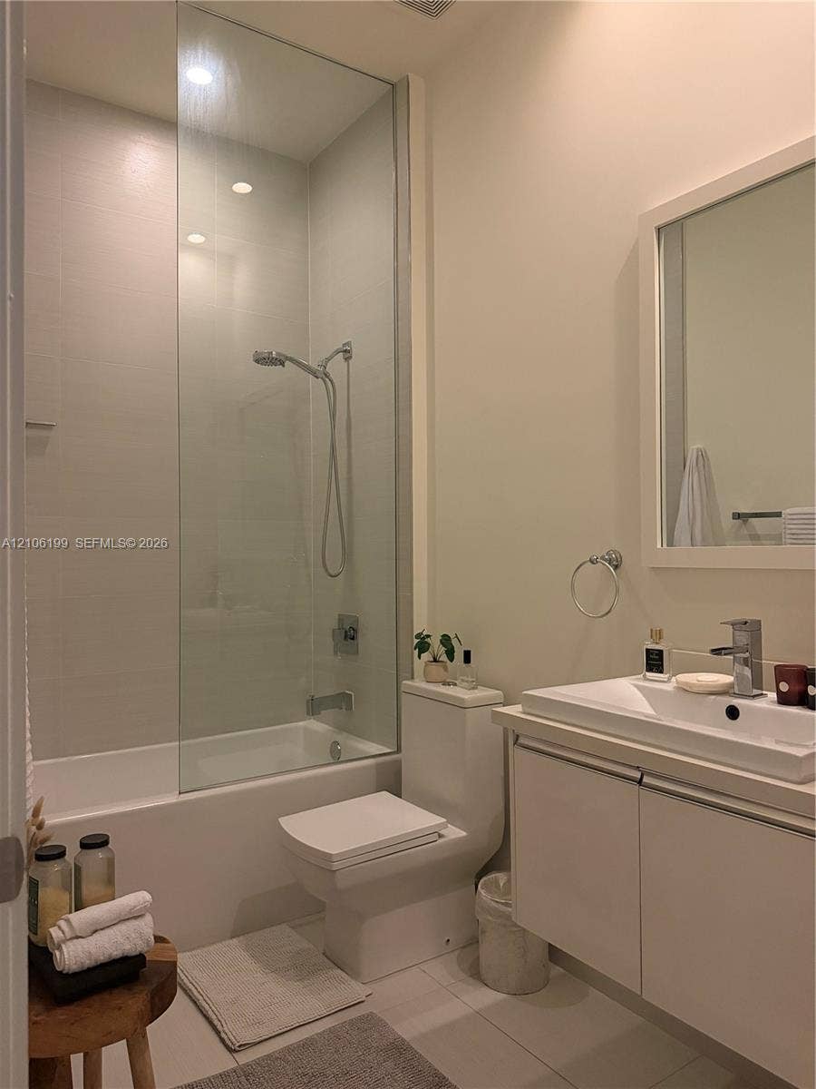 Full-height glass shower panel, integrated bathtub, vanity with rectangular basin, wall-mounted mirror, and tile flooring