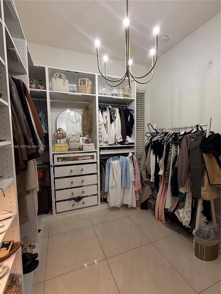 Custom storage system featuring floor-to-ceiling white cabinetry, integrated drawers with gold-tone hardware, polished tile flooring, and a multi-arm metallic chandelier