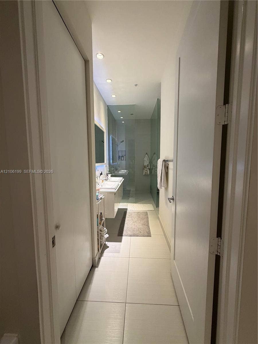 Bathroom featuring large-format floor tile, floating dual-sink vanity, recessed ceiling lighting, and a glass-enclosed shower