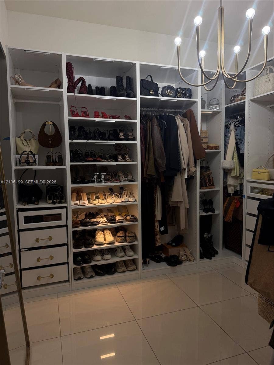 Custom built-in storage system featuring floor-to-ceiling white cabinetry, integrated shelving, pull-out drawers with metallic hardware, and a multi-arm modern light fixture over tile flooring