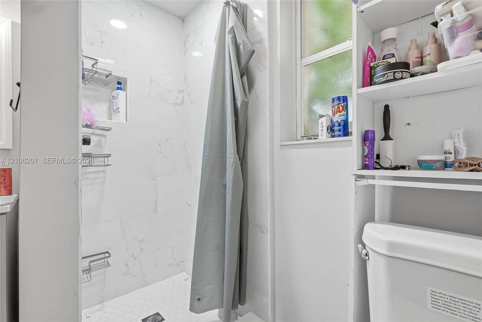 Shower enclosure featuring large-format white stone-finish wall tile, a recessed storage niche, and a hexagonal tile floor