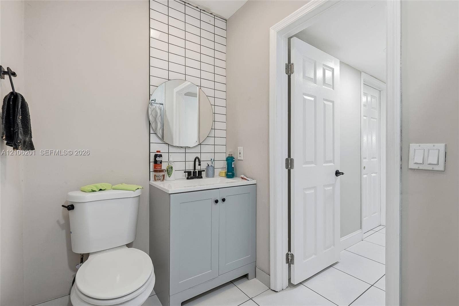 Bathroom featuring a light blue vanity, rectangular white sink with a matte black faucet, circular wall-mounted mirror, and vertical white tiled backsplash