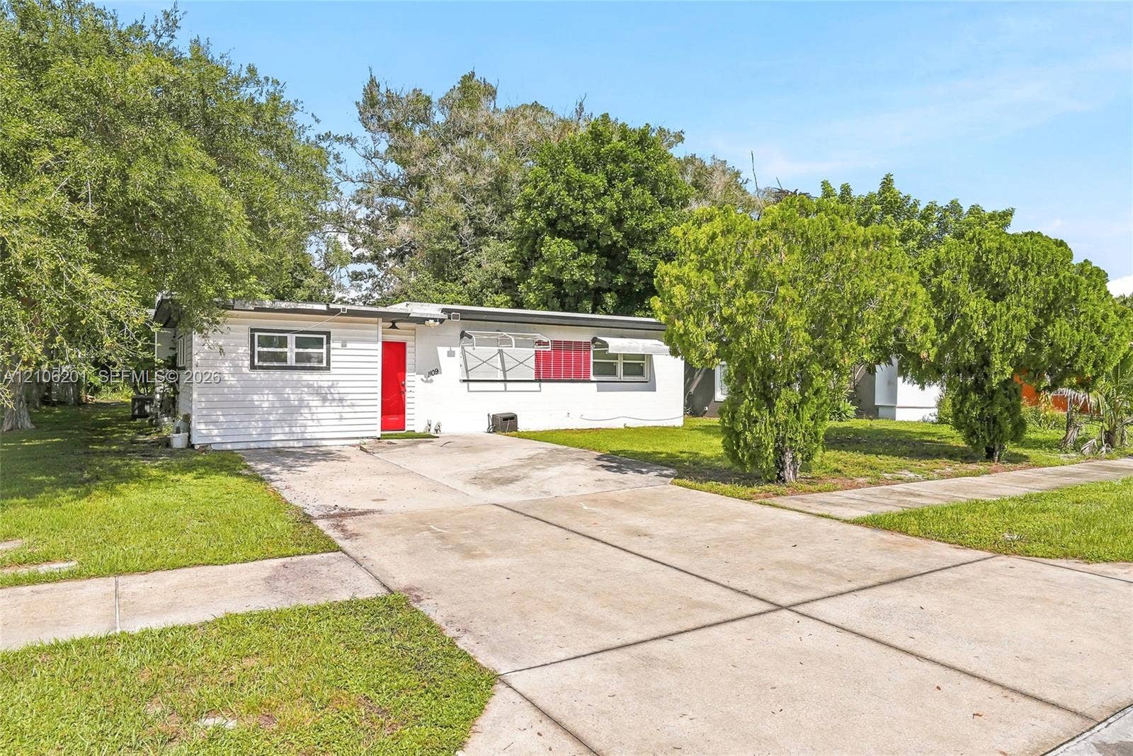 Single-story exterior featuring white horizontal siding, a vibrant red front door, aluminum window awnings, and a concrete driveway