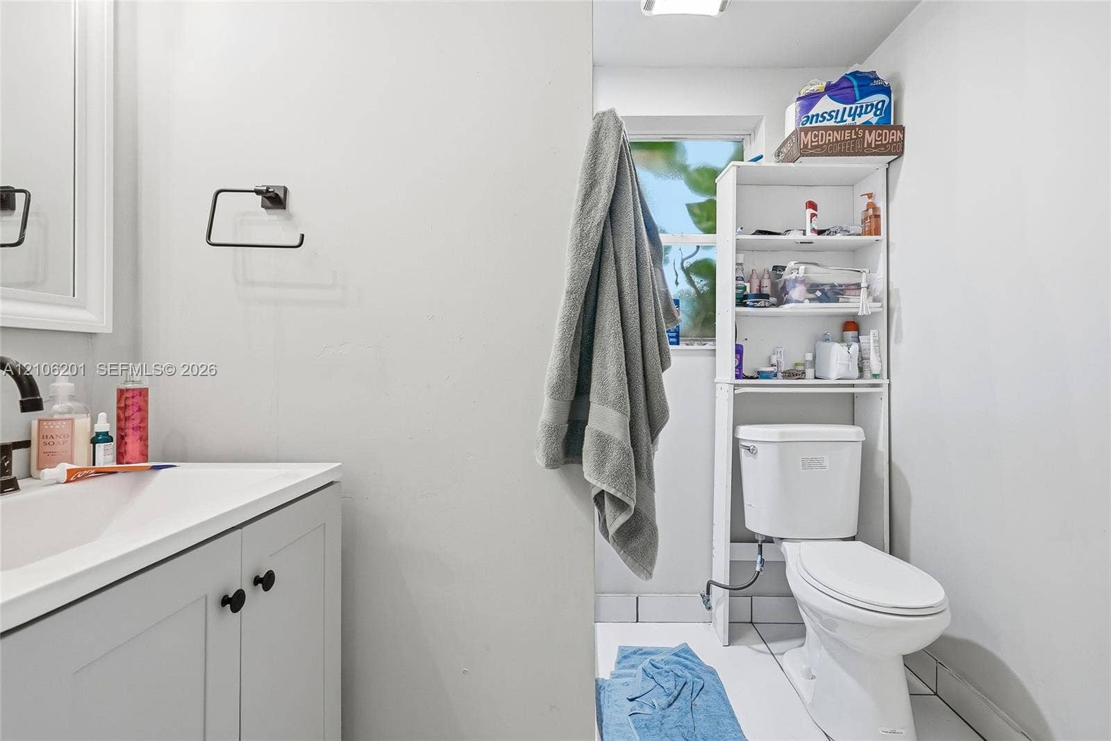 Bathroom featuring a white vanity cabinet, a rectangular sink basin, a metal faucet, a wall-mounted toilet, and a window