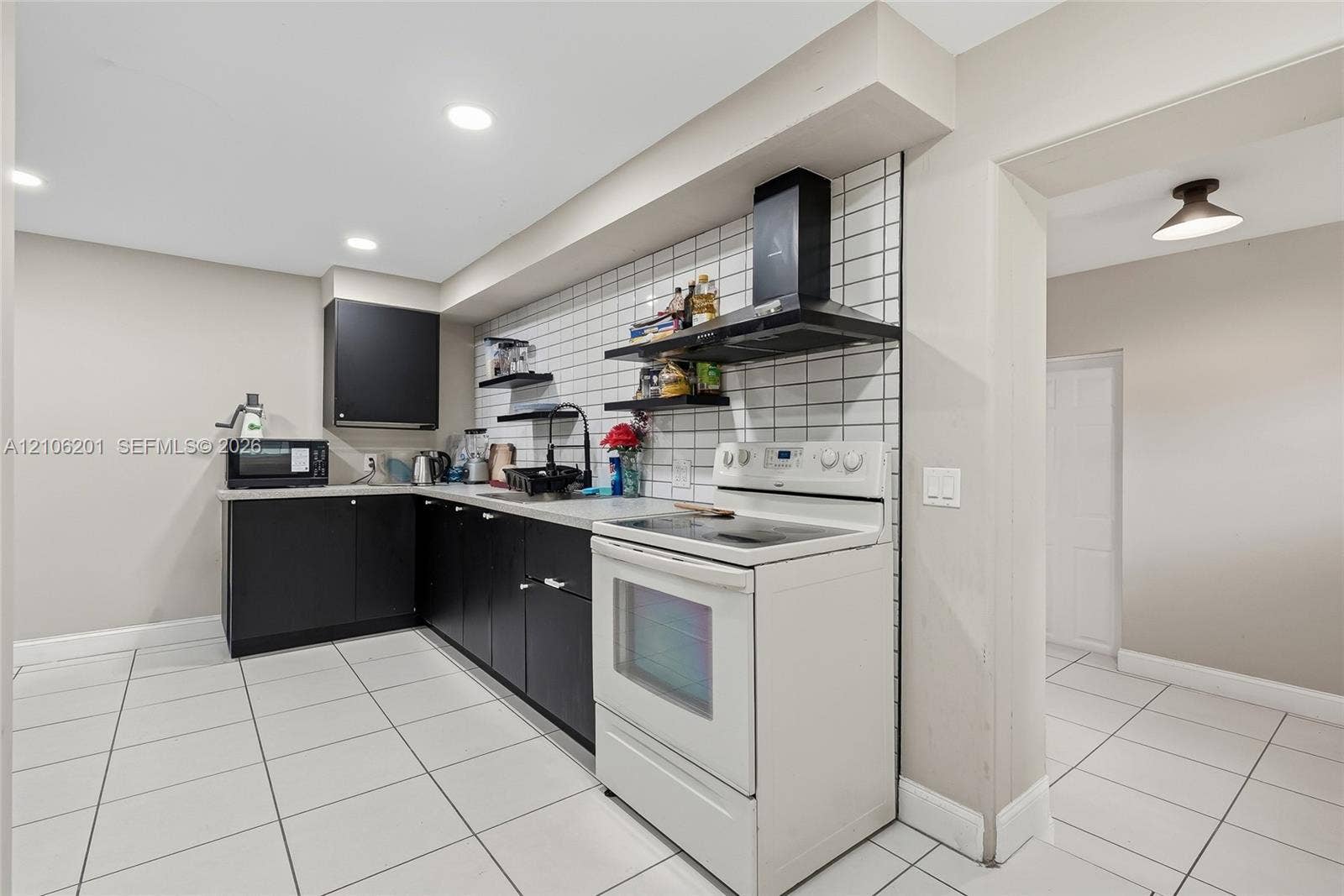 Kitchen featuring matte black cabinetry, white square tile backsplash, white ceramic tile flooring, built-in black range hood, and recessed lighting