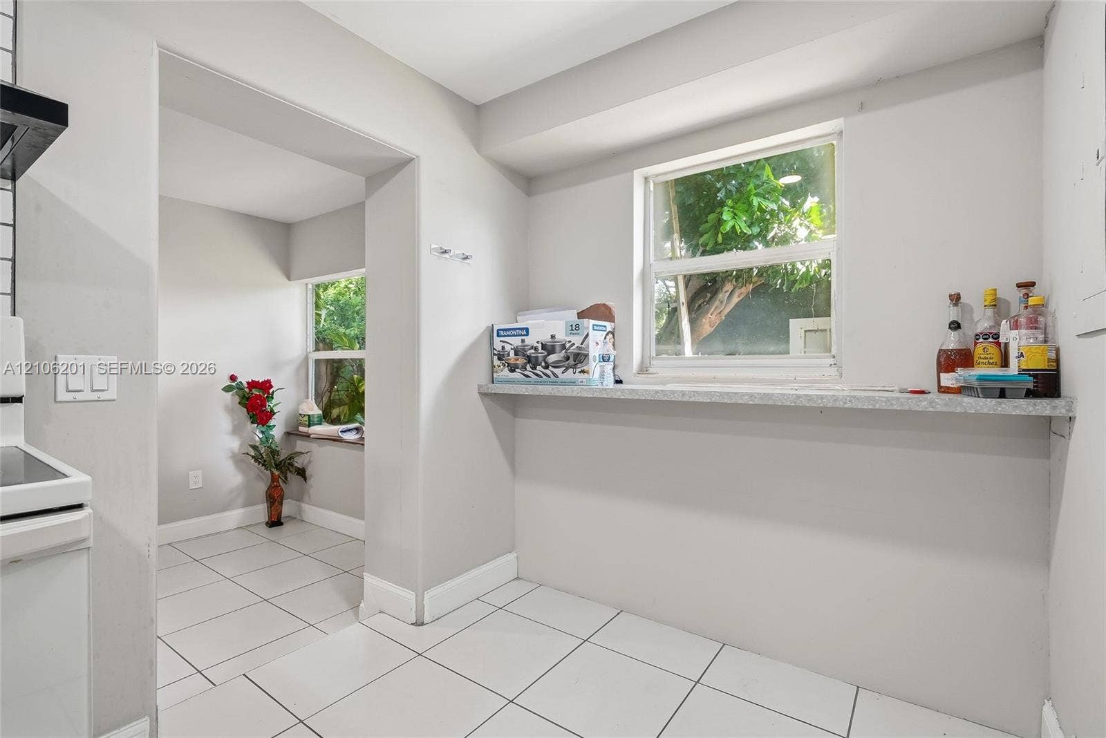 Kitchen area featuring white ceramic tile flooring, light-toned walls, and a built-in stone-finish ledge under a window