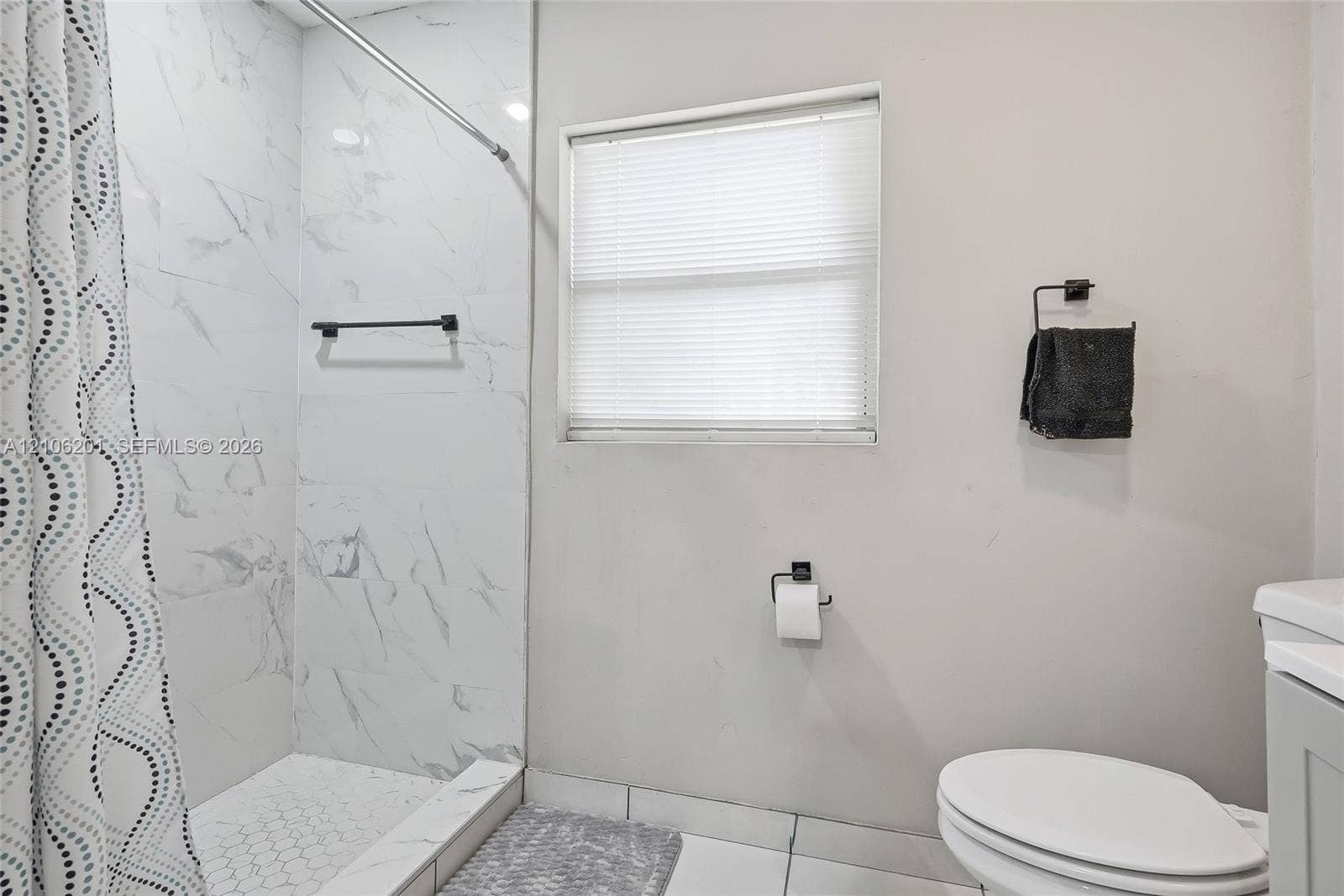 Full-height shower surround with stone-patterned tile, white hexagonal tile shower flooring, recessed window with blinds, and matte black hardware